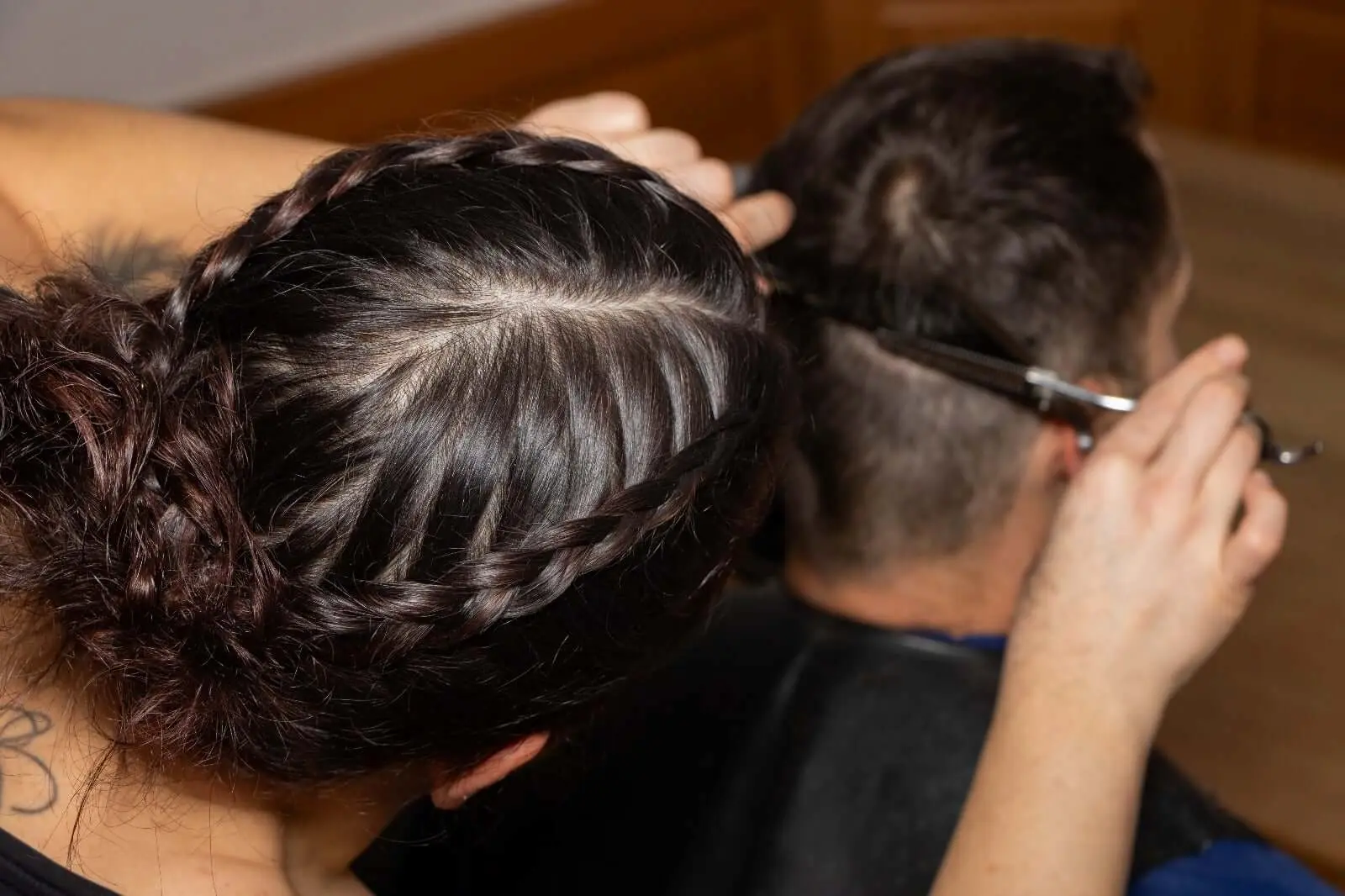 Friseuse schneidet einem Mann die braunen Haare mit einer Schere und Kamm