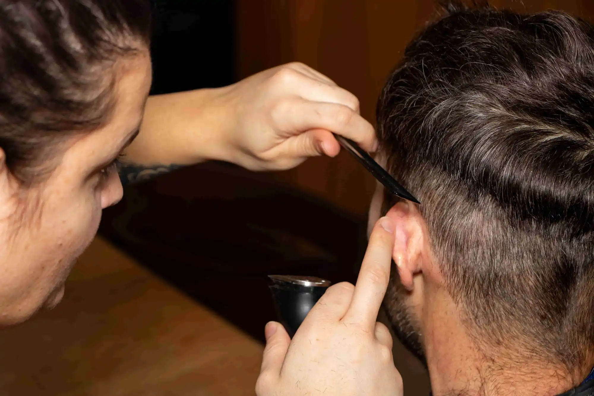 Friseuse schneidet einem Mann die Konturen hinter dem Ohr mit Schere und Rasierer